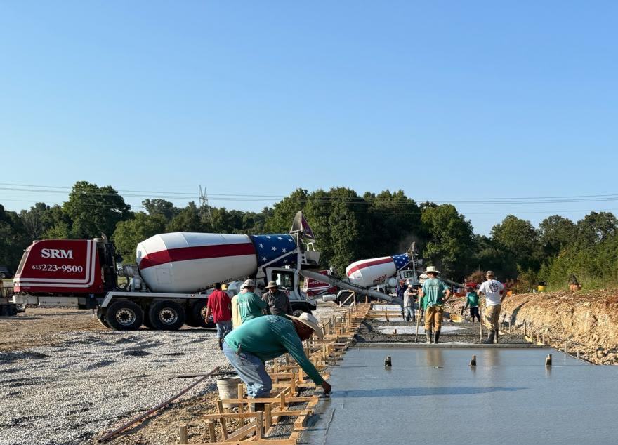 Concrete crew finishing a foundation slab at the True Blue site while mixer trucks pour