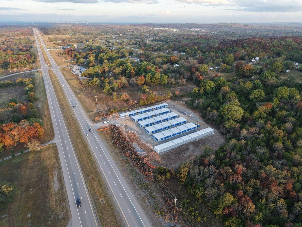 Aerial view along John Bragg Highway showing all six buildings with blue doors, surrounded by fall trees